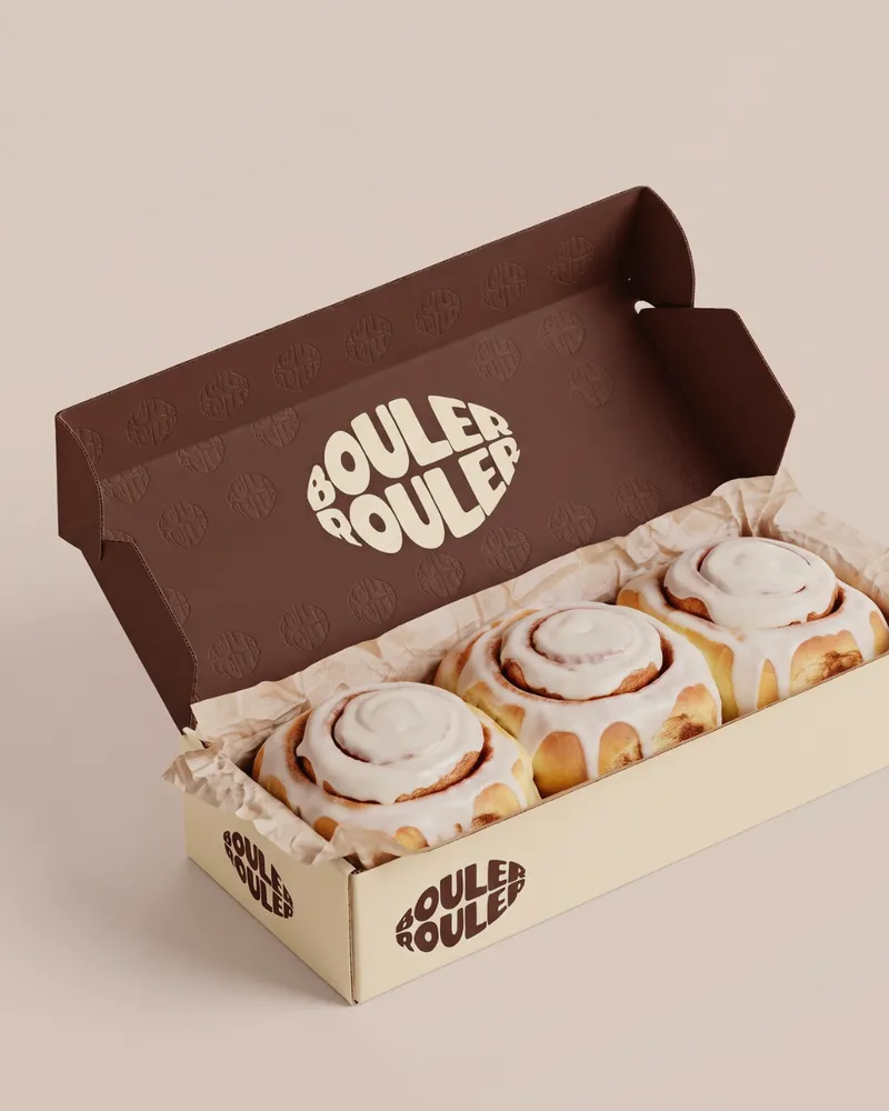 Boîte ouverte avec trois cinnamon rolls glacés, couvercle brun gaufré du logo