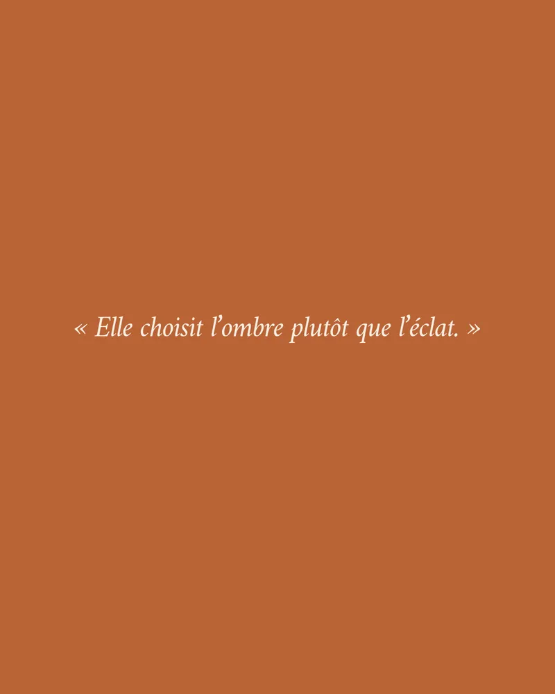 La phrase « Elle choisit l’ombre plutôt que l’éclat. » en italique crème sur fond terre cuite
