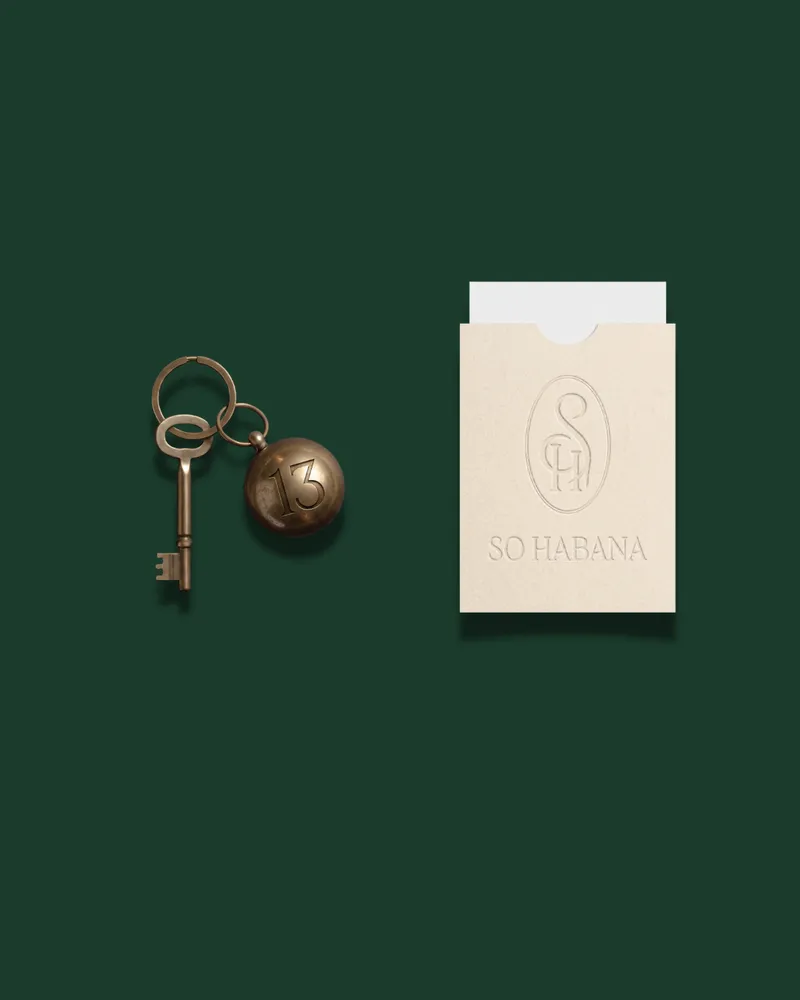 Une clé ancienne avec un porte-clé en laiton numéroté 13, à côté d’une pochette crème au monogramme gaufré